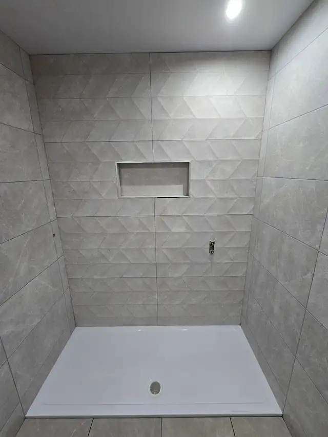 Walk-in shower tiled in large grey geometric tiles with a recessed niche