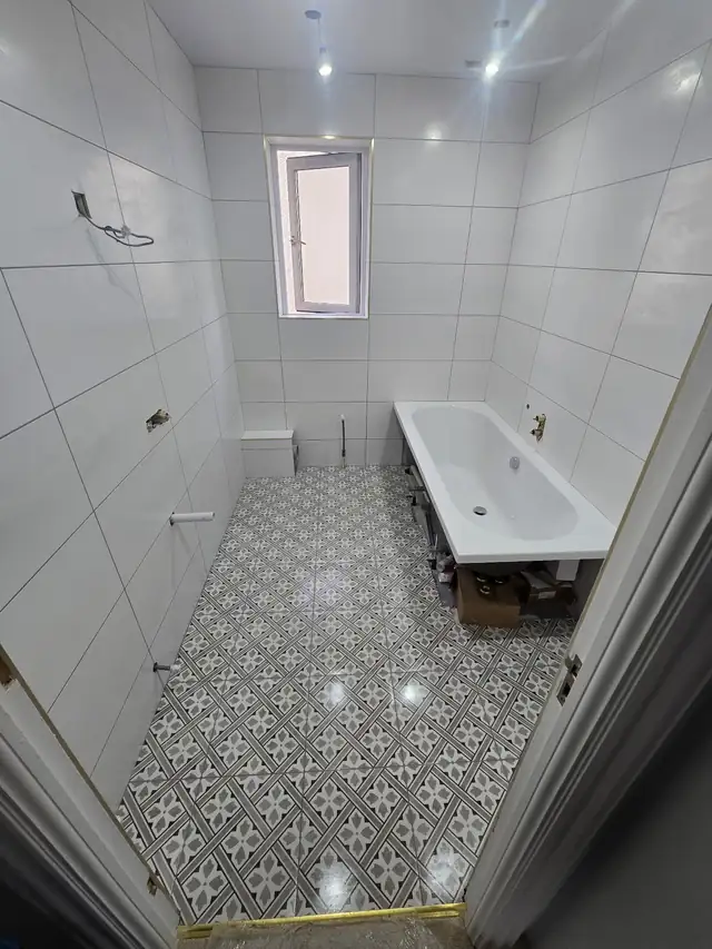 Bathroom with white wall tiles and a grey and white patterned floor, tiled by CKP Tiling