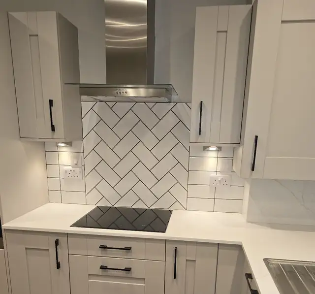 White herringbone metro tile splashback behind a black hob in a shaker kitchen